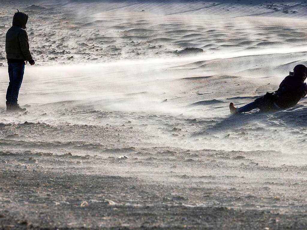 Eine Frau liegt im Sandsturm am Strand von Warnemnde und fotografiert.