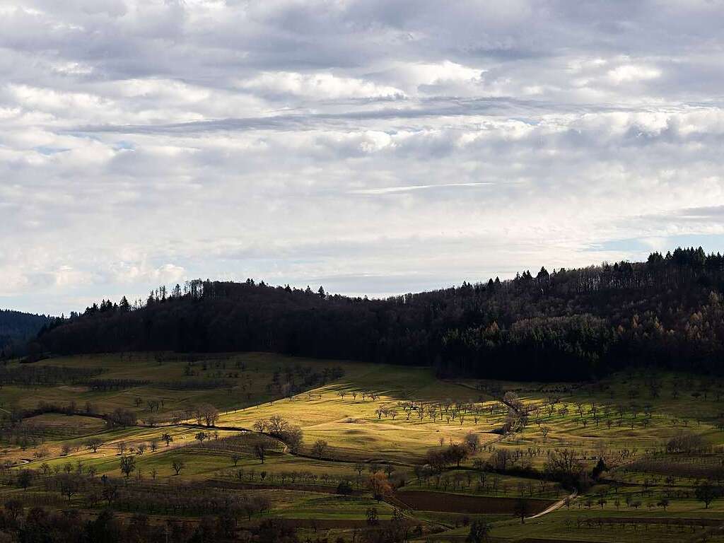 Ein Fleck Sonnenlicht fllt auf Felder und Bume unterhalb eines Waldstcks bei Schliengen im Markgrflerland. Der Sdwesten Deutschlands blieb bisher vor schweren Strmen verschont.