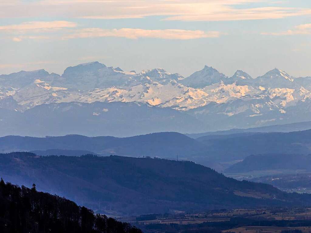 Die schneebedeckten Hnge der Alpen sind im Hintergrund zu erkennen whrend im Vordergrund die dunklen Hhenzge des Schwarzwalds bei Schliengen zu sehen sind.