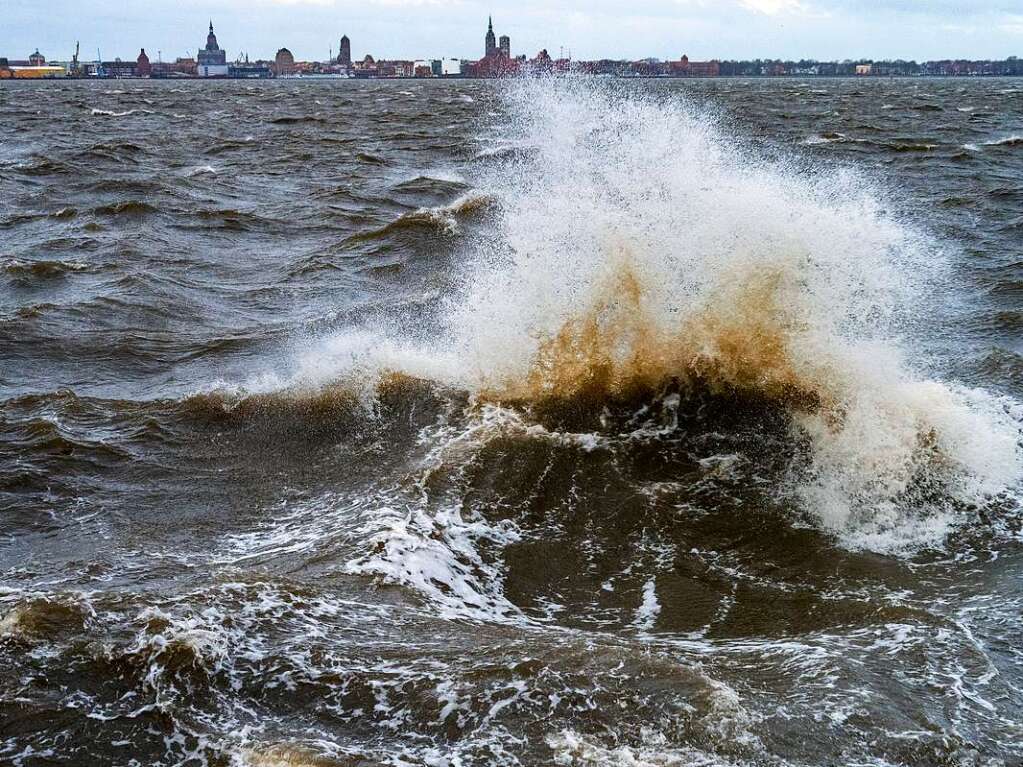 Wellen brechen sich am Strand von Altefhr auf der Insel Rgen. Im Hintergrund ist die Silhouette der Hansestadt Stralsund zu sehen.