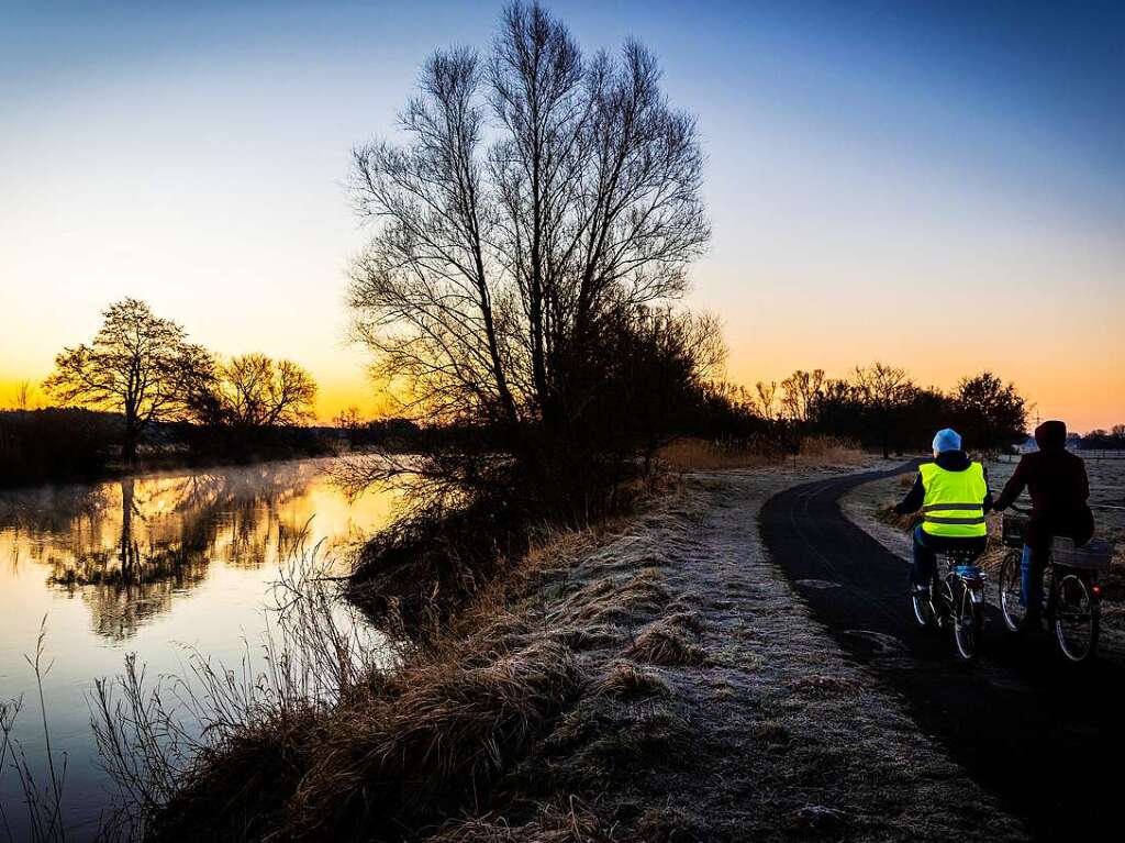 Celle: Radfahrer fahren im Licht der aufgehenden Sonne eine Allee im Franzsischen Garten entlang.