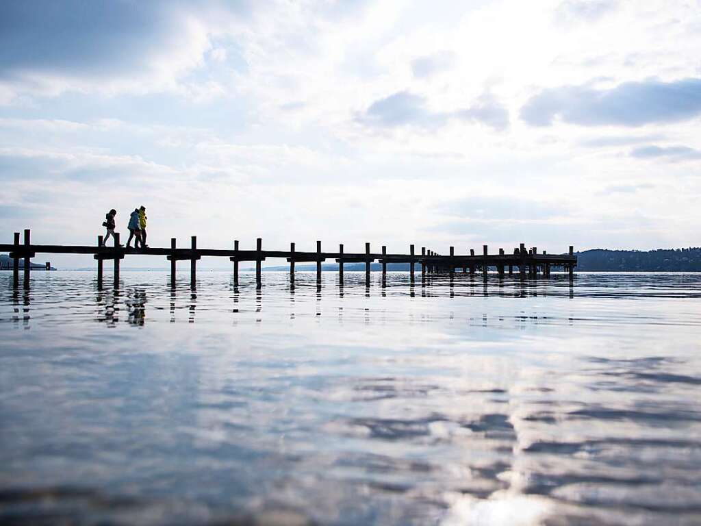 Percha: Menschen genieen am Starnberger See das schne Wetter auf einem Steg.