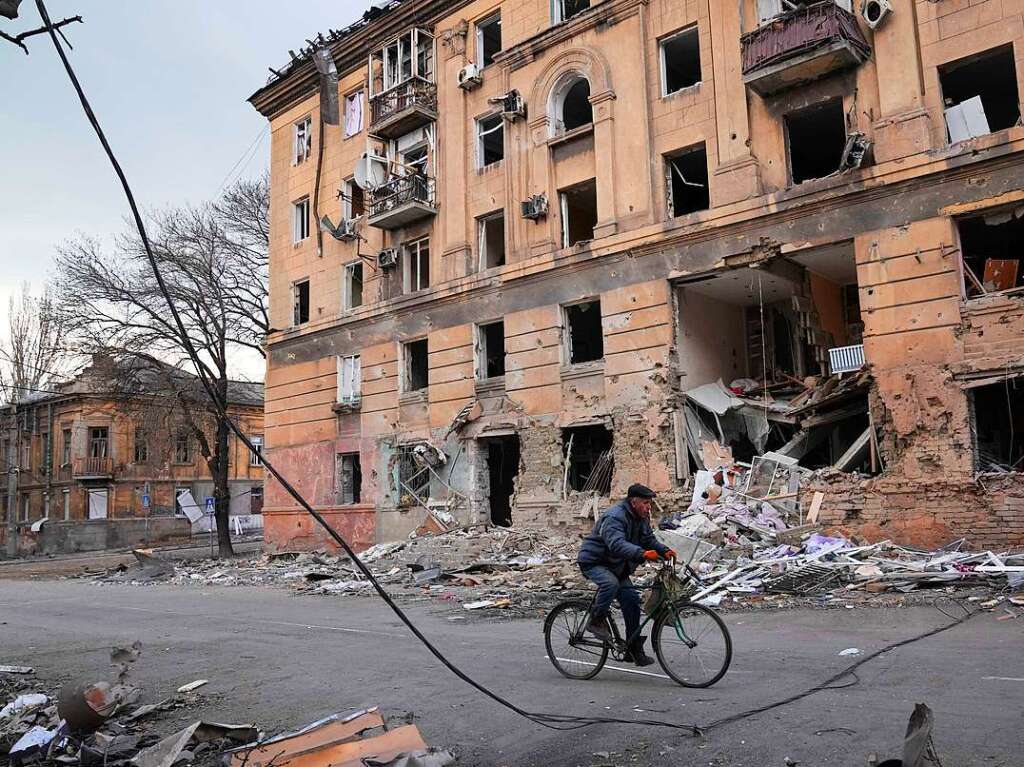 Ein Mann fhrt mit dem Fahrrad an einem durch einen Angriff beschdigten Wohnhaus in Mariupol vorbei.