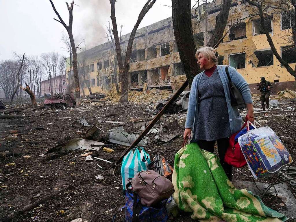 Eine Frau steht mit ihrem Gepck vor einer durch einen Angriff beschdigten Geburtsklinik in Mariupol.