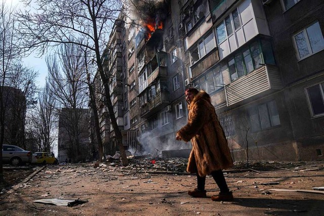 Eine Frau geht an einem brennenden Woh...ntag, 13. Mrz 2022, beschossen wurde.  | Foto: Evgeniy Maloletka (dpa)
