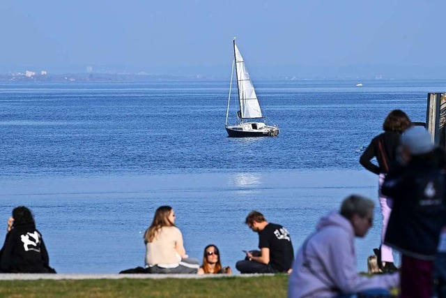 Menschen sitzen an der Uferpromenade, ...nd im Bodensee ein Boot vorbei segelt.  | Foto: Felix Kstle (dpa)