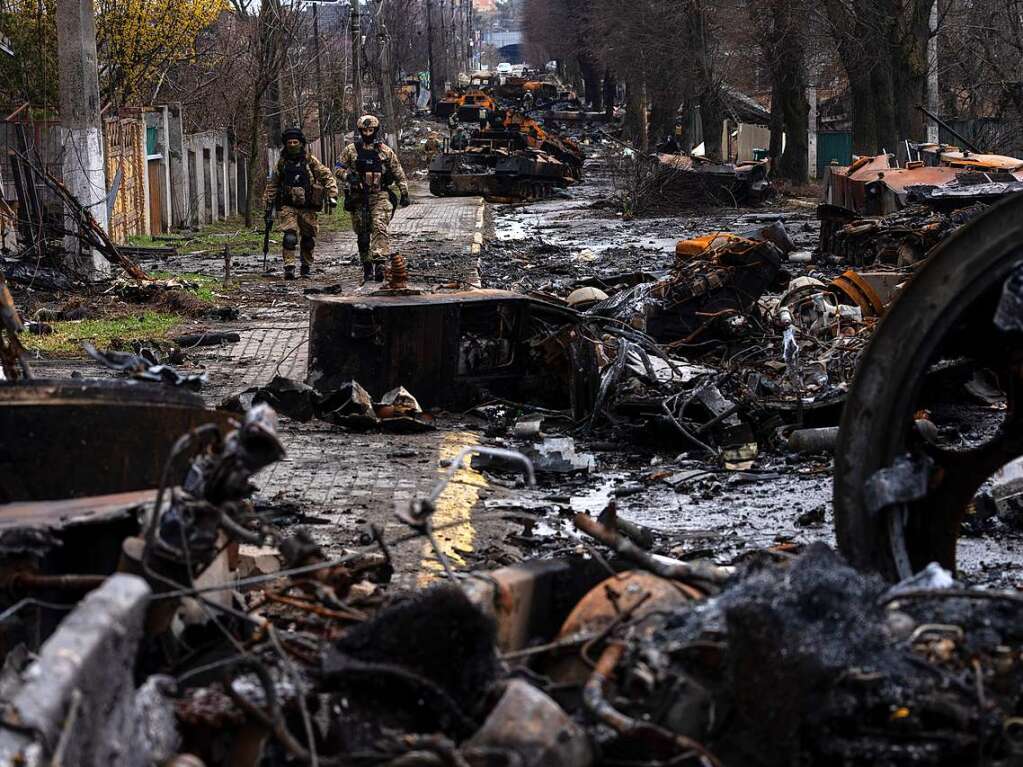 Zwei ukrainische Soldaten gehen auf einer Strae, die berst ist mit zerstrten russischen Militrfahrzeugen.