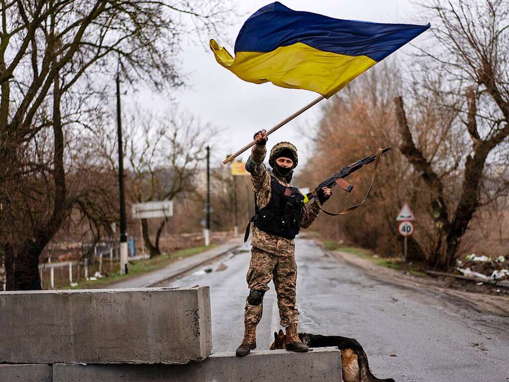 Ein ukrainischer Soldat steht an einer Straenblockade und hlt die ukrainische Flagge hoch.