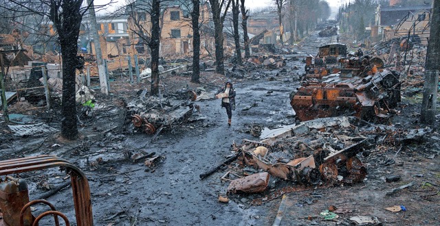 Eine Frau geht auf einer Strae in But...rstrten russischen Militrfahrzeugen.  | Foto: Rodrigo Abd (dpa)