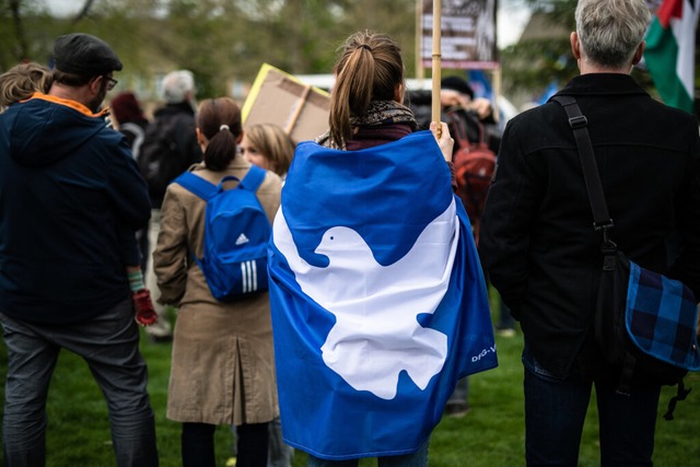 Eine Teilnehmerin eines Ostermarsches ...Flagge mit einer Friedenstaube darauf.  | Foto: Christoph Schmidt (dpa)