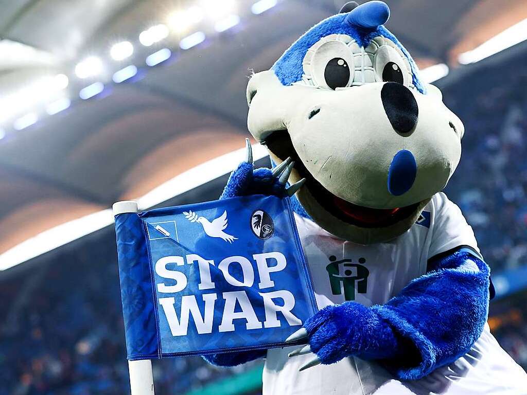 Dino Hermann, Maskottchen des Hamburger SV, hlt eine Eckfahne mit Friedenstaube und dem Schriftzug "STOP WAR".