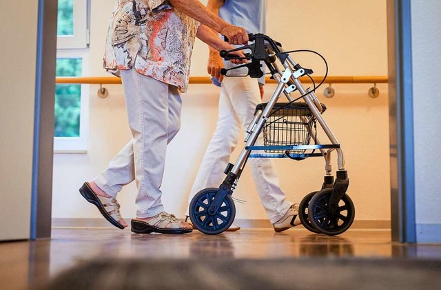 Eine Pflegekraft geht in einem Pflegeh...iner lteren Dame ber einen Korridor.  | Foto: Christoph Schmidt (dpa)