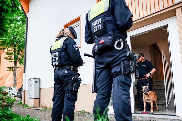 Ein Polizist mit Sprhund steht im Hauseingang des Tatverdchtigen in Essen.  | Foto: Fabian Strauch (dpa)