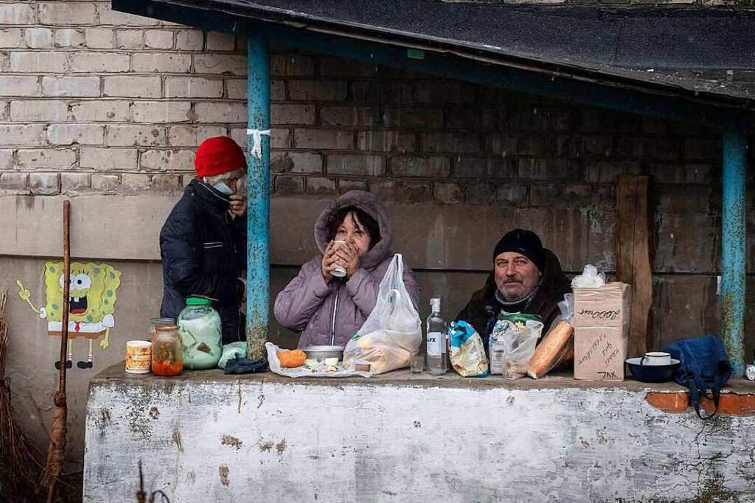 Eine Bewohnerin und ein Bewohner der o...t, essen vor einem zerstörten Gebäude.  | Foto: IMAGO/Valery Melnikov