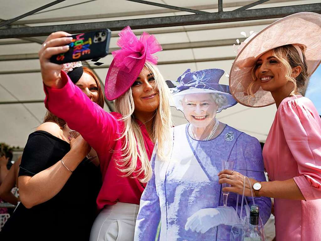 Besucher machen vor dem Ladies Day des Cazoo Derby Festival 2022 auf der Pferderennbahn von Epsom ein Selfie mit einem Pappausschnitt der Queen