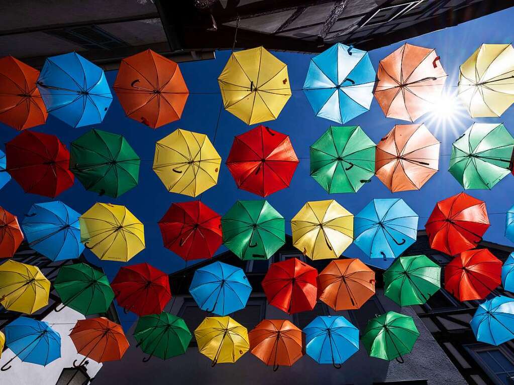 Die Sonne scheint in der Altstadt von Bdingen, Hessen, zwischen dutzenden bunter Schirme hindurch, die dort zwischen den Husern zu einer Installation aufgespannt wurden