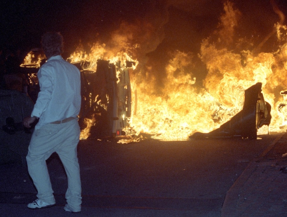 Ein Mann steht vor einem brennenden Pk...ostock-Lichtenhagen. (Archivbild 1992)  | Foto: Bernd Wüstneck