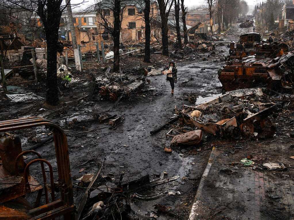 Eine Frau geht in Butscha am Stadtrand von Kiew auf einer Strae, die berst ist mit zerstrten russischen Militrfahrzeugen.