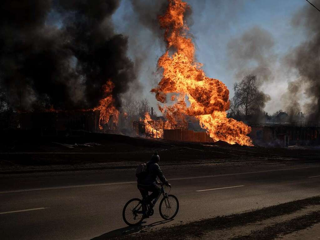 Ein Mann fhrt mit seinem Fahrrad an Flammen und Rauch vorbei, die von einem Feuer nach einem russischen Angriff aufsteigen.