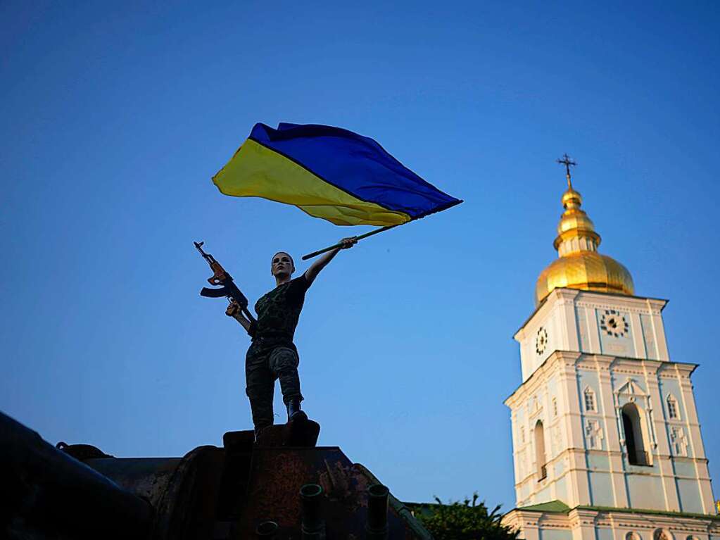 Eine Frau schwenkt die ukrainische Flagge auf einem zerstrten russischen Panzer.