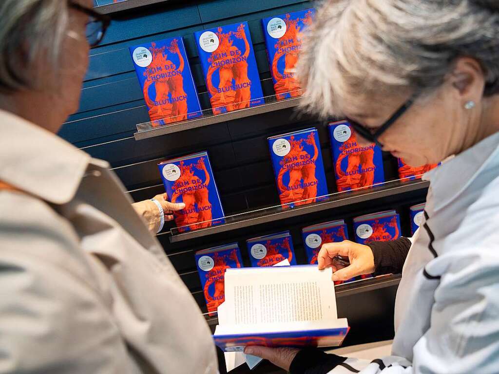 Besucherinnen schauen auf der Frankfurter Buchmesse am Stand des DuMont Buchverlags Ausgaben von Blutbuch von Kim de l'Horizon, das den Deutschen Buchpreis 2022 gewonnen hat, an.