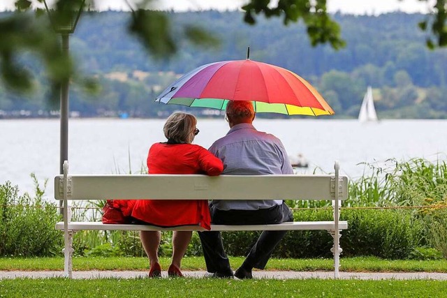 Ein Seniorenpaar sitzt in berlingen a...see auf einer Bank unter einem Schirm.  | Foto: Thomas Warnack (dpa)
