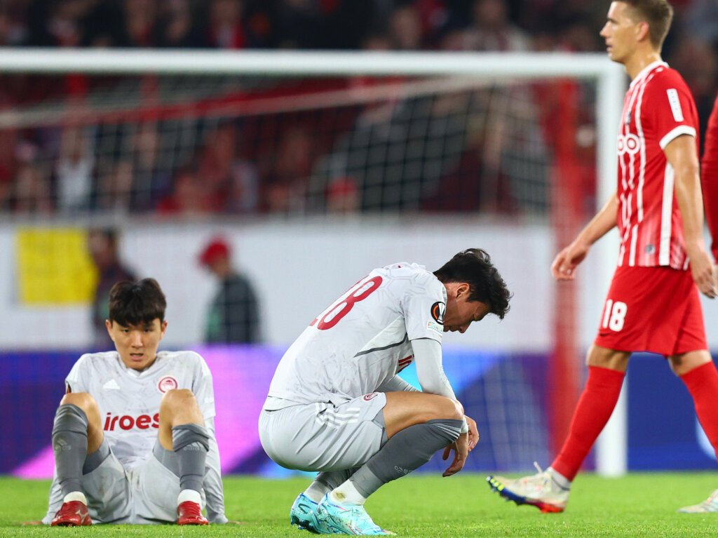 Pirus' In-beom Hwang (l) und Pirus' Ui-jo Hwang hocken nach dem Spiel auf dem Rasen, Freiburgs Nils Petersen geht dahinter vorbei.