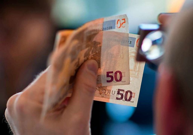 Achtung, Falschgeld: Ein Mitarbeiter d...t mit der Lupe zwei 50-Euro-Banknoten.  | Foto: Andreas Arnold (dpa)