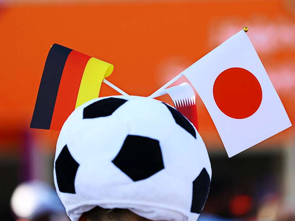 Die Kopfbedeckung eines Zuschauers als Fussball ist mit einer japanischen und eiuem deutschen Fhnchen verziert.