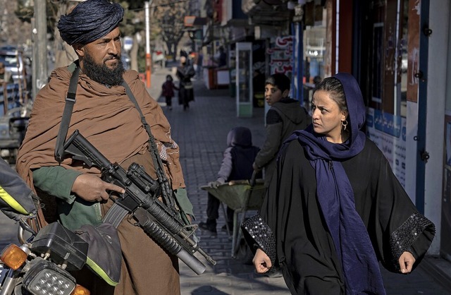 Ein Taliban-Kmpfer steht Wache, whre...e Frau vorbeiluft und ihn  mustert.    | Foto: Ebrahim Noroozi (dpa)