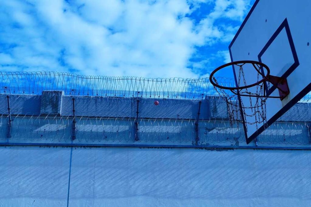 Ein Basketball hängt im Stacheldraht der Gefängnismauern.  | Foto: Lisa Discher