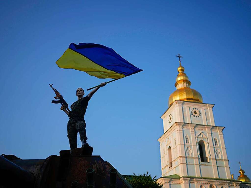 Eine Frau schwenkt die ukrainische Flagge auf einem zerstrten russischen Panzer.