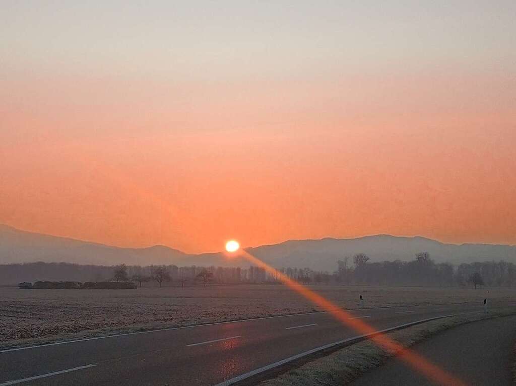 Die blutorange Winter-Sonne steigt hinter dem Berg auf.