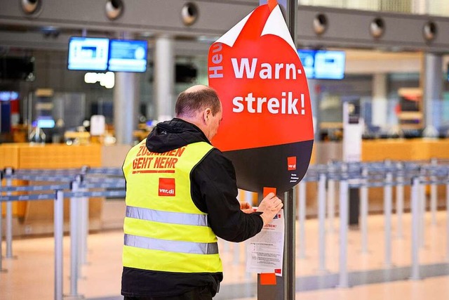 Ein Gewerkschaftsvertreter klebt ein P...n Terminal 2 des Hamburger Flughafens.  | Foto: Jonas Walzberg (dpa)