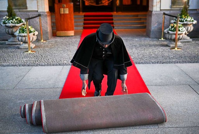 Berlin: Doorman Timothy Uhunamure roll...dem Hotel Adlon den roten Teppich aus.  | Foto: Jens Kalaene (dpa)