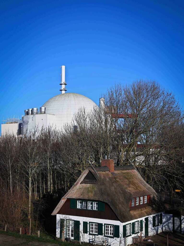 Die Kuppel des Reaktorgebudes des Kernkraftwerks Brokdorf in Schleswig-Holstein ist hinter einem Reetdachhaus am Elbdeich zu sehen. Nach knapp 35 Jahren Betriebszeit wurde das Atomkraftwerk Ende 2021 abgeschaltet.