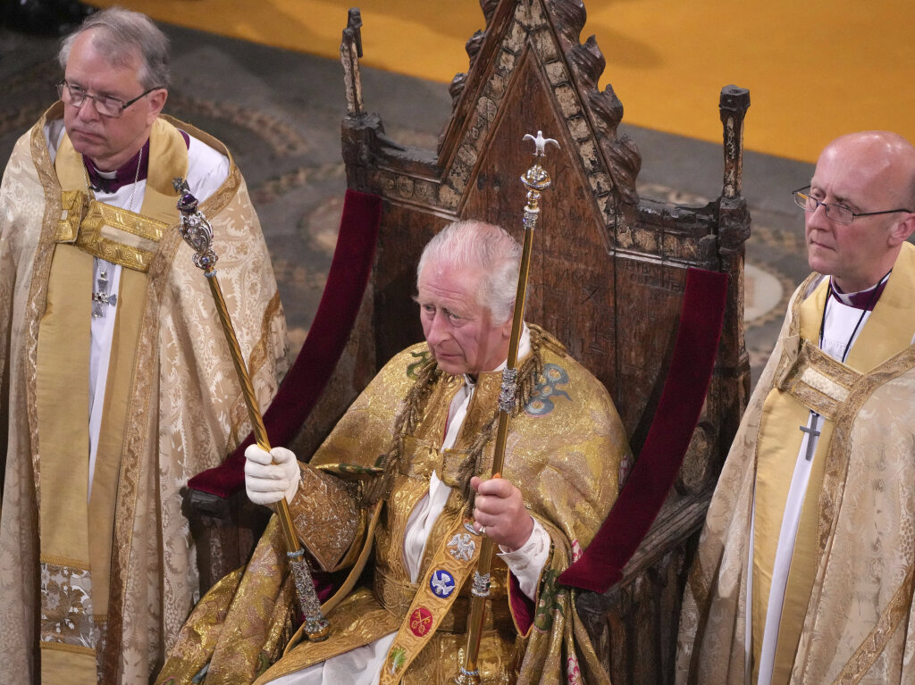 Knig Charles III. (M) sitzt whrend der Krnungszeremonie in der Westminster Abbey mit zwei Zeptern auf dem Thron.