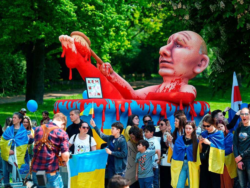 Teilnehmer einer Demonstration gegen Proteste gegen Waffenlieferungen in die Ukraine stehen vor einer Karnevalsfigur vom russischen Prsidenten Putin in einem Blutbad aus dem Rosenmontagszug in Dsseldorf.