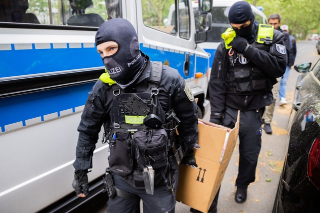 Polizisten tragen bei einer Hausdurchs...uzberg einen Karton zu einem Fahrzeug.  | Foto: Christoph Soeder (dpa)