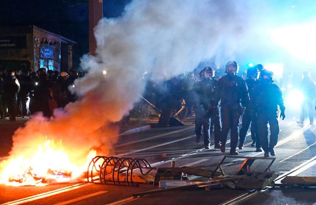 Polizisten gehen an einer brennenden Barrikade vorbei.  | Foto: Sebastian Willnow (dpa)