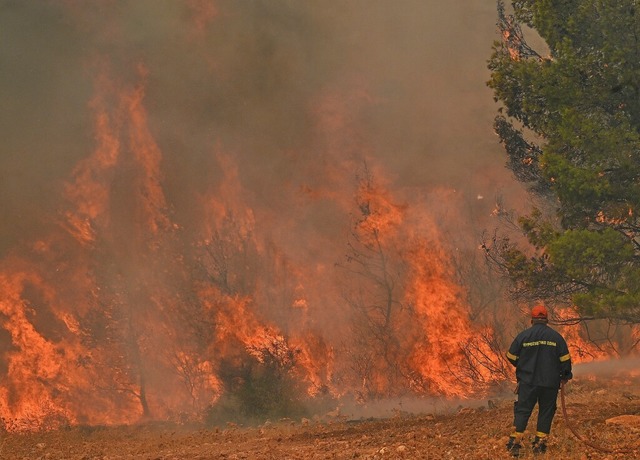 Ein Feuerwehrmann steht vor den Flamme...s Brandes im griechischen Nea Peramos.  | Foto: LOUISA GOULIAMAKI