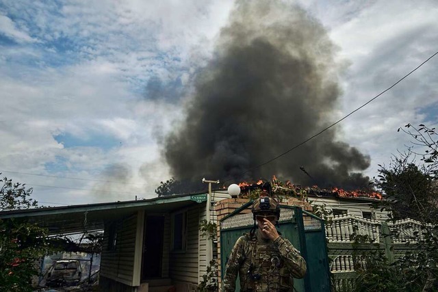 Ein ukrainischer Soldat steht vor einem brennenden Haus in Frontnhe.  | Foto: LIBKOS (dpa)