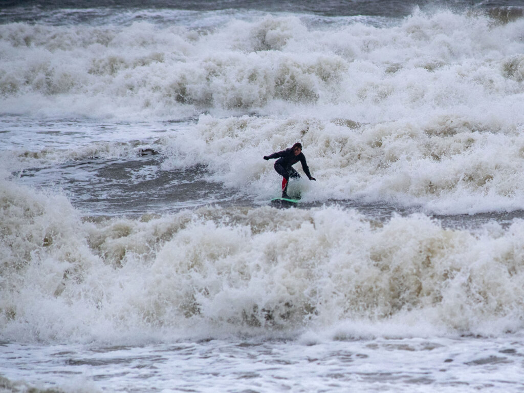 In Binz in Mecklenburg-Vorpommern traut sich ein Surfer in die tosenden Wellen in der Ostsee