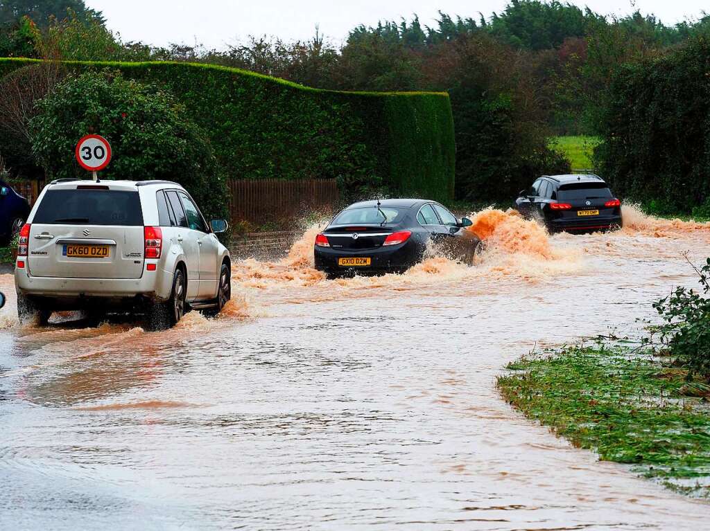 Grobritannien, Yapton: Fahrzeuge fahren durch eine berflutete Strae.