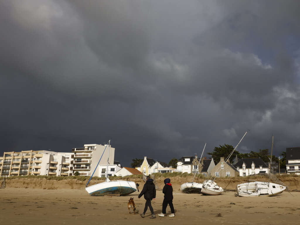 Frankreich, Pornichet: Ein Paar geht an angeschwemmten Booten am Strand in der Bretagne vorbei.