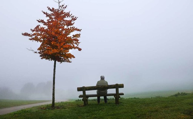 Eine Frau sitzt an einem Aussichtspunkt im Nebel auf einer Bank.  | Foto: Thomas Warnack (dpa)