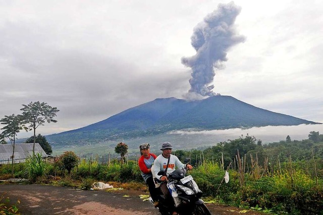 Rollerfahrer fahren vorbei, als der Be...ruchs vulkanisches Material ausspuckt.  | Foto: Ardhy Fernando (dpa)