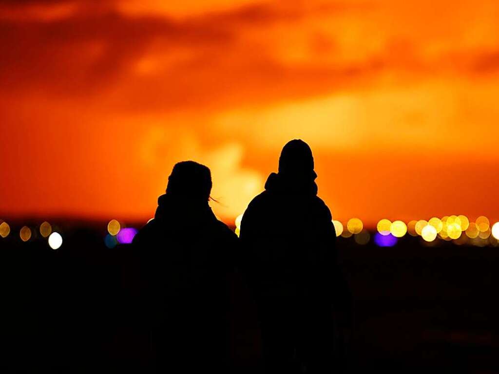 Menschen in Reykjavik beobachten, wie der Nachthimmel nach dem Ausbruch eines Vulkans erhellt wird.