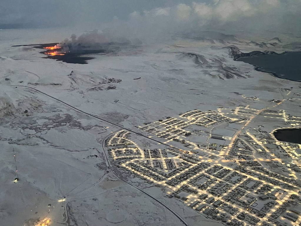 Die evakuierte Stadt Grindavik im Vordergrund, die Eruption im Hintergrund.