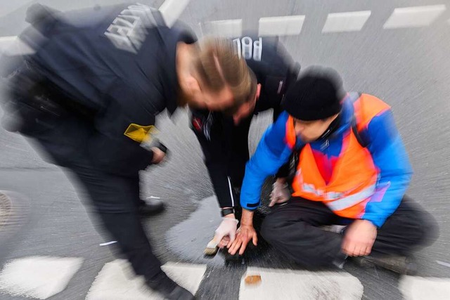 Polizisten versuchen festgeklebte Hnd...mit Speisel von der Strae abzulsen.  | Foto: Julian Stratenschulte (dpa)